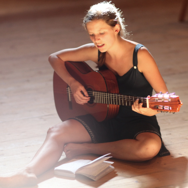 Eine Frau sitzt auf dem Boden, singt und spielt Gitarre