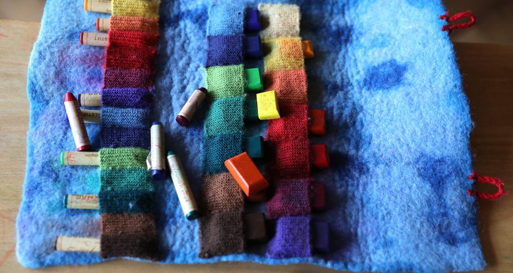 In einem blauen Filzkoffer sind verschiedene Blöcke und Stifte mit bunter, pastellfarbener Kreide aufgerollt, einige ordentlich in Fächern untergebracht, andere verstreut auf einer hölzernen Unterlage liegend.